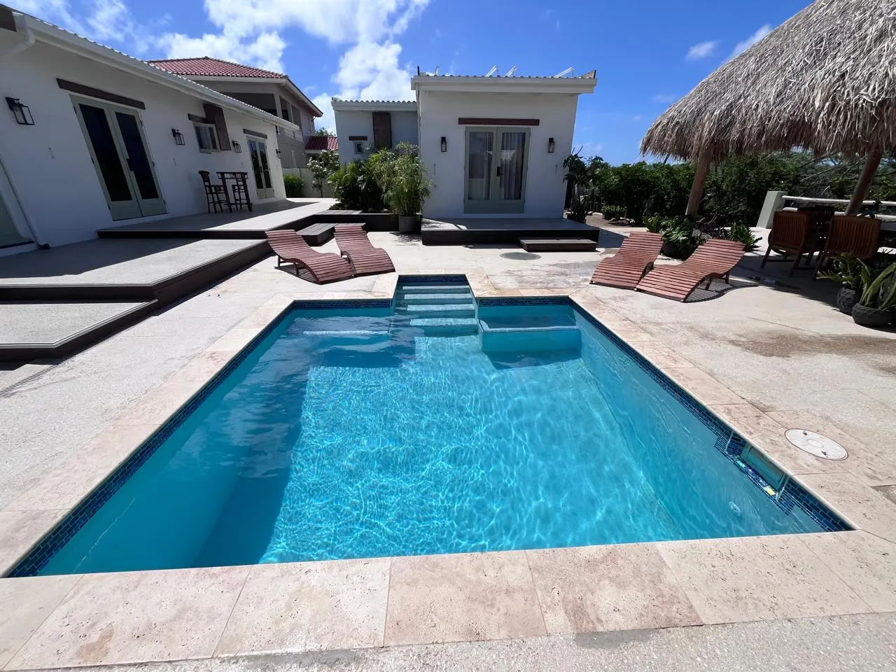 Pool with sun loungers and a thatched palapa in the background